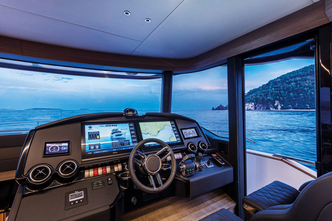 The helm station, with twin displays, the wheel and wide forward glazing onto the sea.