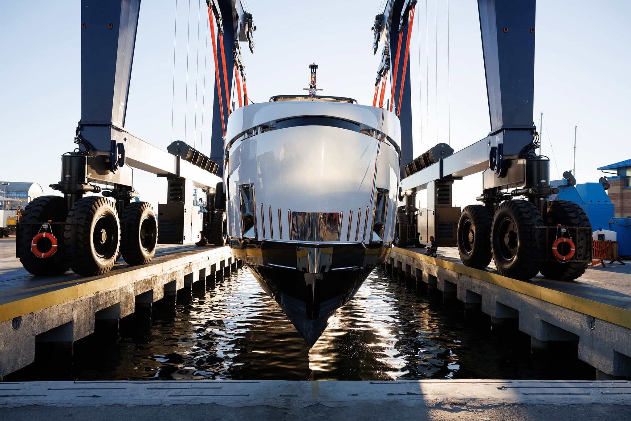 The first Magellano 27M seen bow on in the travel lift at the moment of launching, her dark antifouling and white topsides reflected in the water of the dock