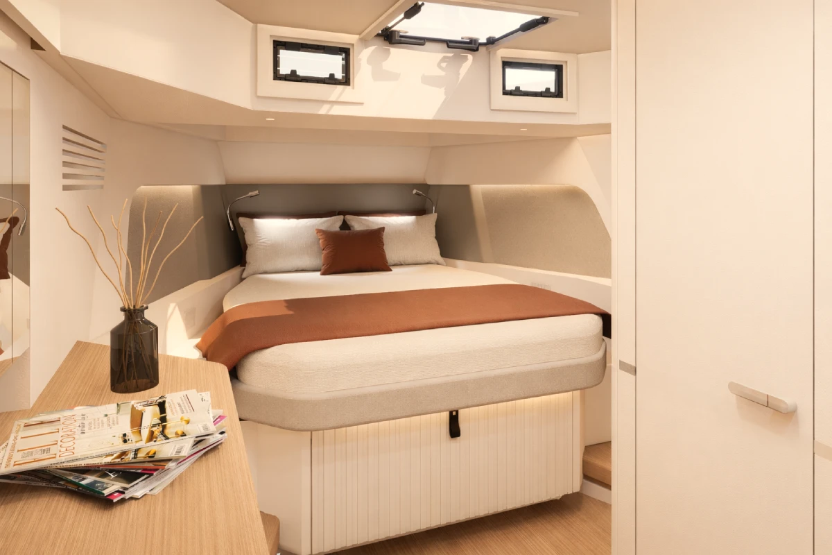 The forward cabin, with a double berth beneath deck hatches and a desk to one side.