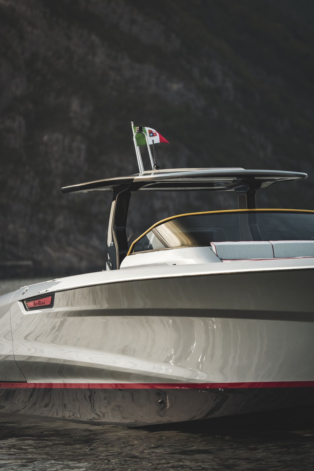 The bow three-quarter view, with the Italian flag at the T-top and the red waterline stripe running forward.