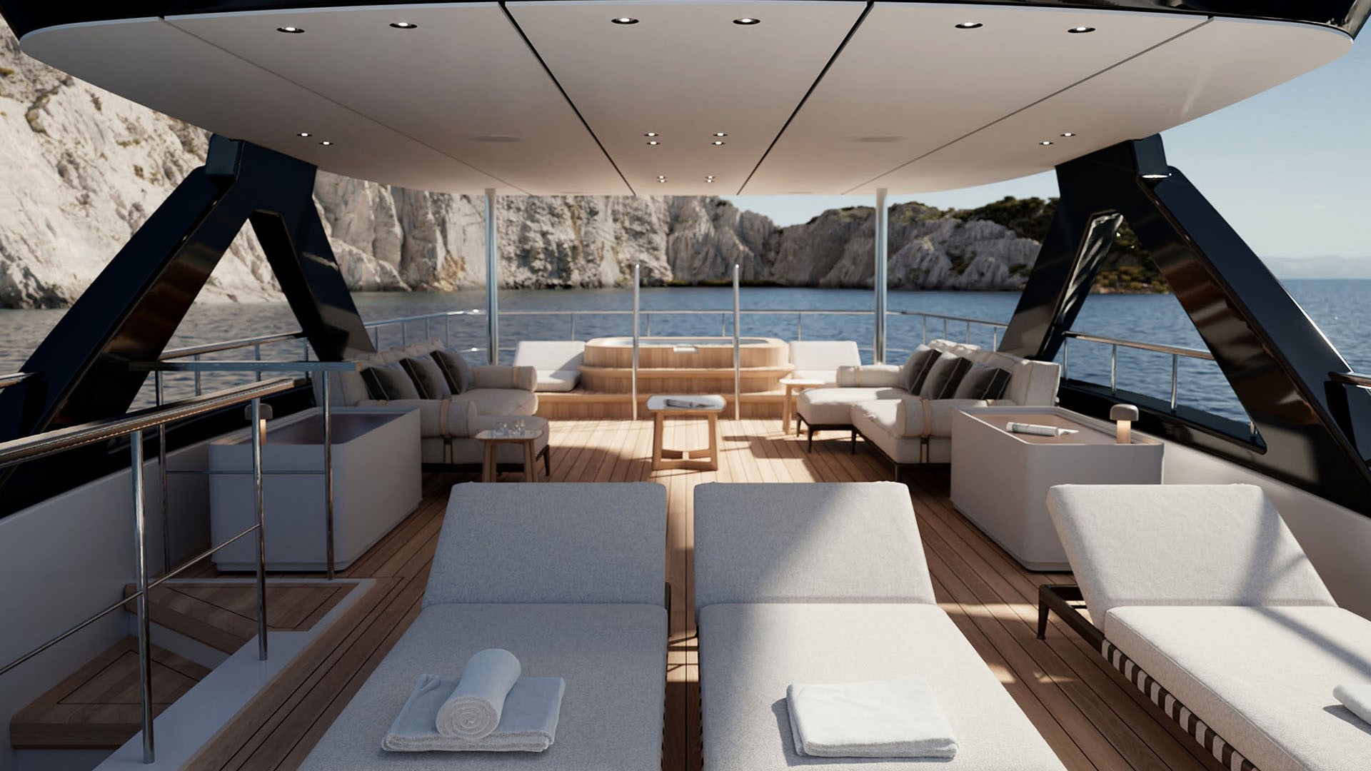 The upper deck looking aft under the hardtop, two loungers in the foreground and sofas either side of a raised circular spa pool, with a limestone cliff astern