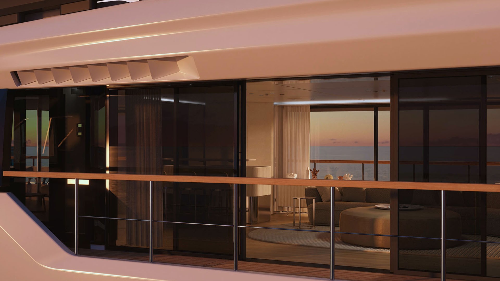 The main deck seen from outside at dusk, warm light spilling through full-height sliding glass onto a teak side deck, with a round sofa and dining area inside