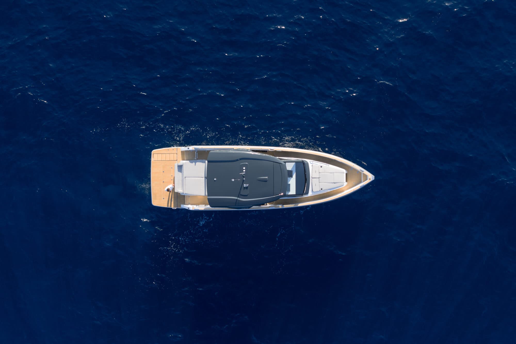The FJORD 440 seen from directly overhead lying still on deep blue water, her teak foredeck and aft platform either side of the dark hardtop over the cockpit