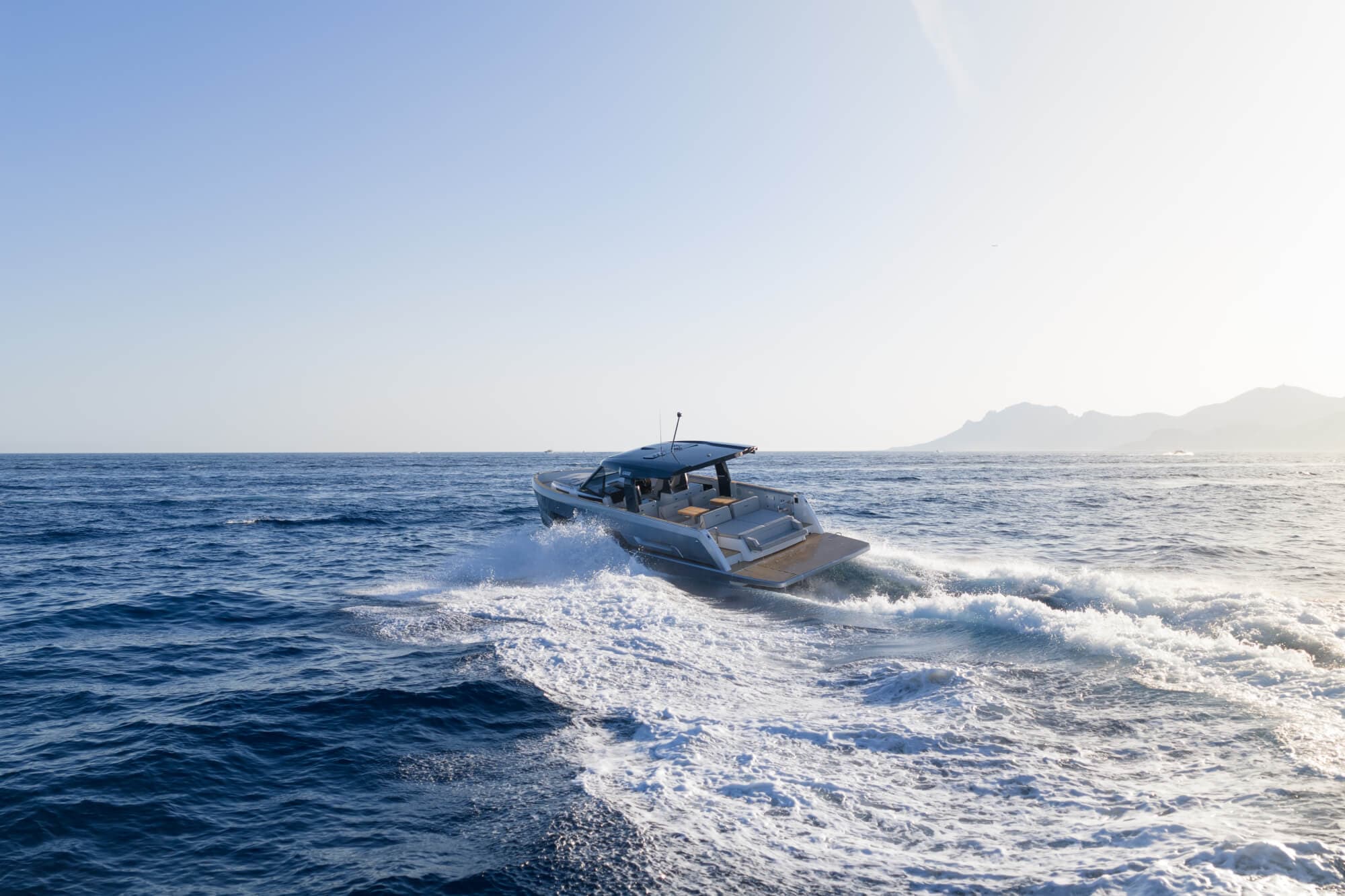 The FJORD 440 running away from the camera into a low sun, her bathing platform and aft sunpad in view and a mountainous coast behind