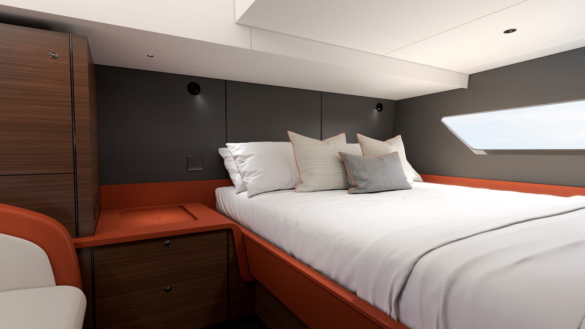 A double cabin below deck, the bed against a dark bulkhead with an orange-trimmed base and shelf, reading lights either side and a long angled hull window above