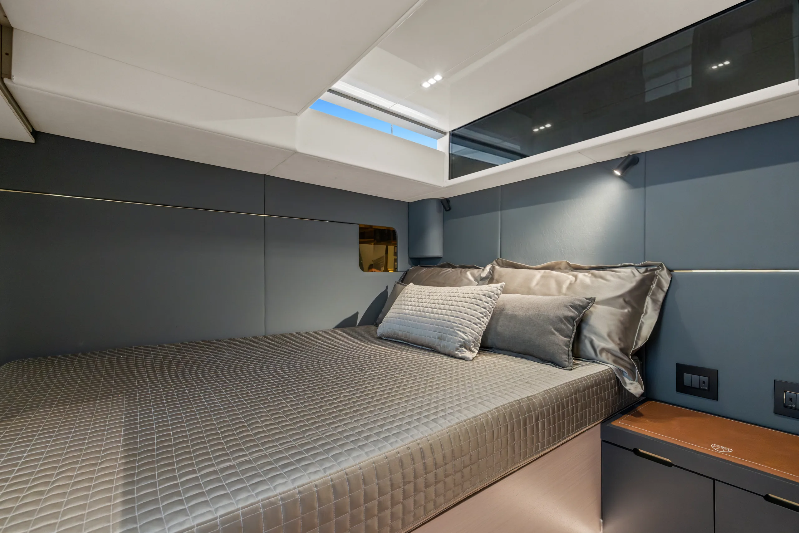 A cabin with a double berth, grey panelling and a hull window