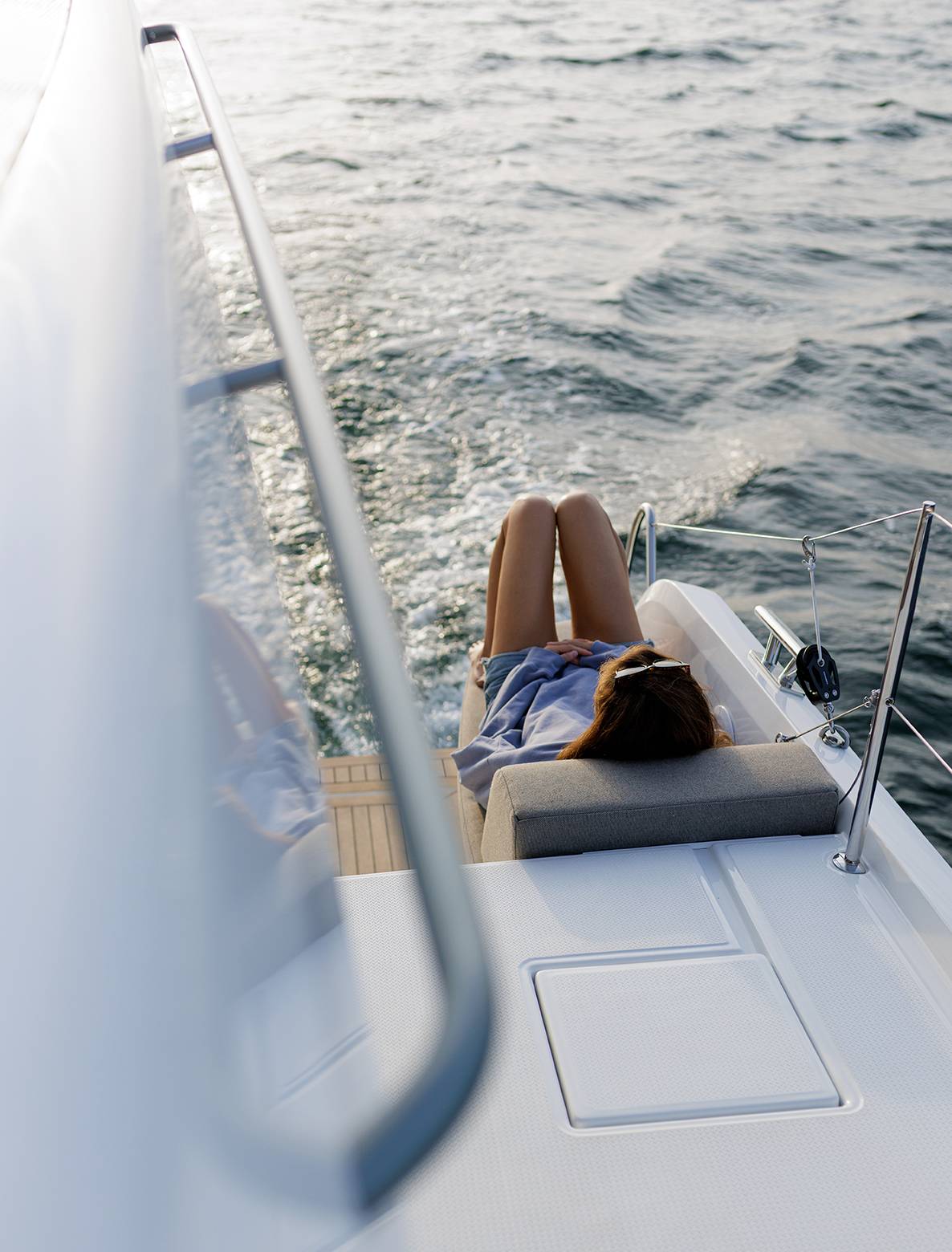 A sunbather on the foredeck lounger seen past the rigging