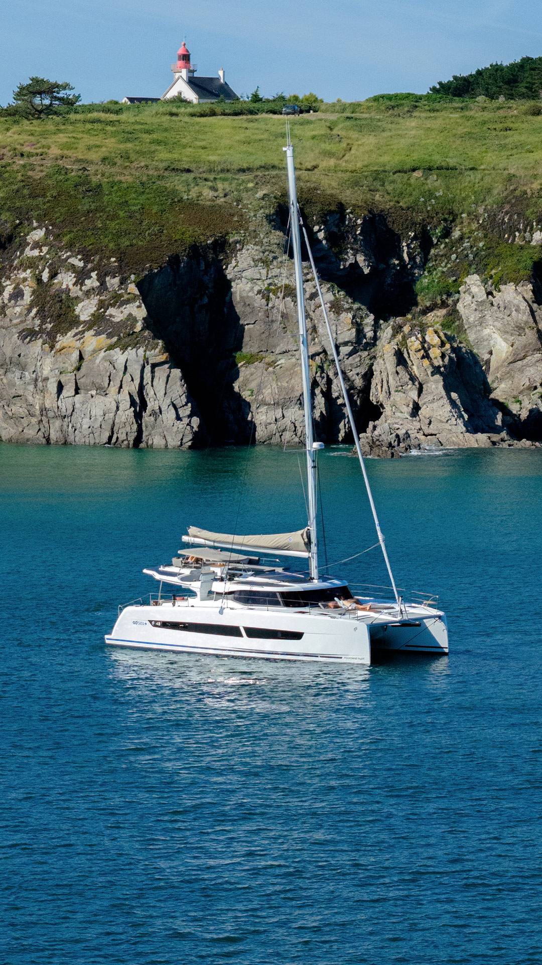 At anchor in a cove below a headland with a lighthouse on top