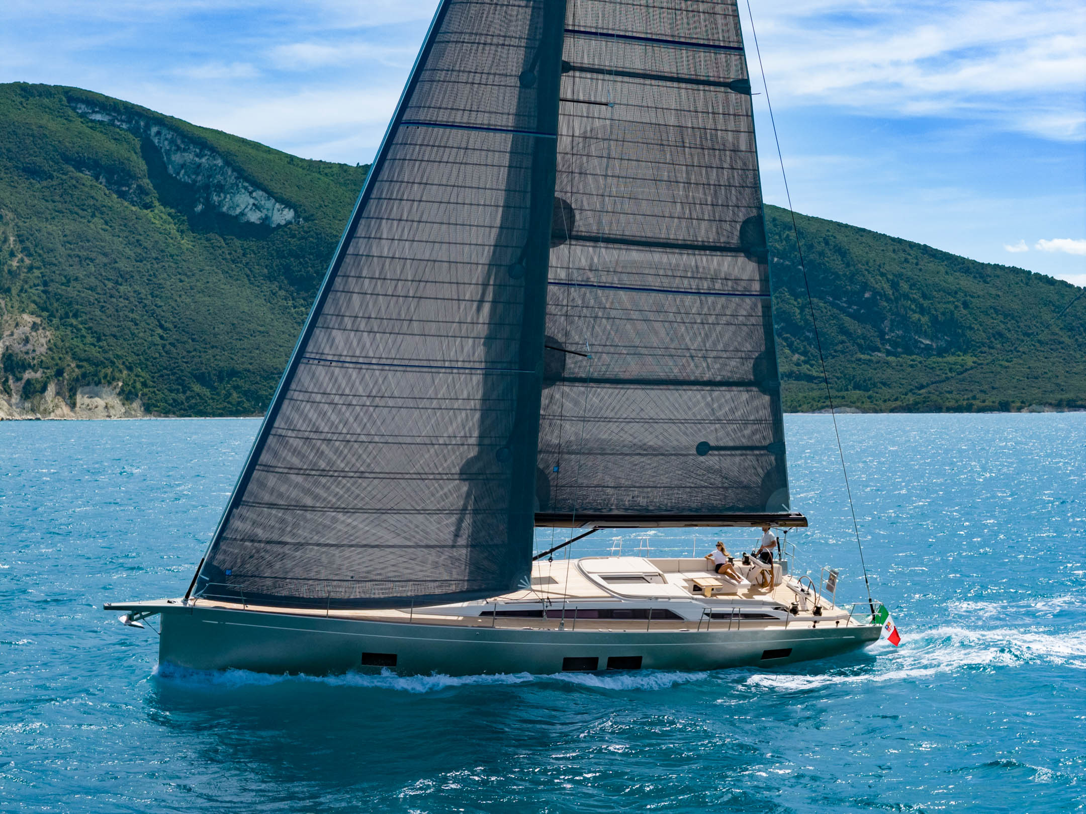 Sailing past a steep green headland with the crew on the rail
