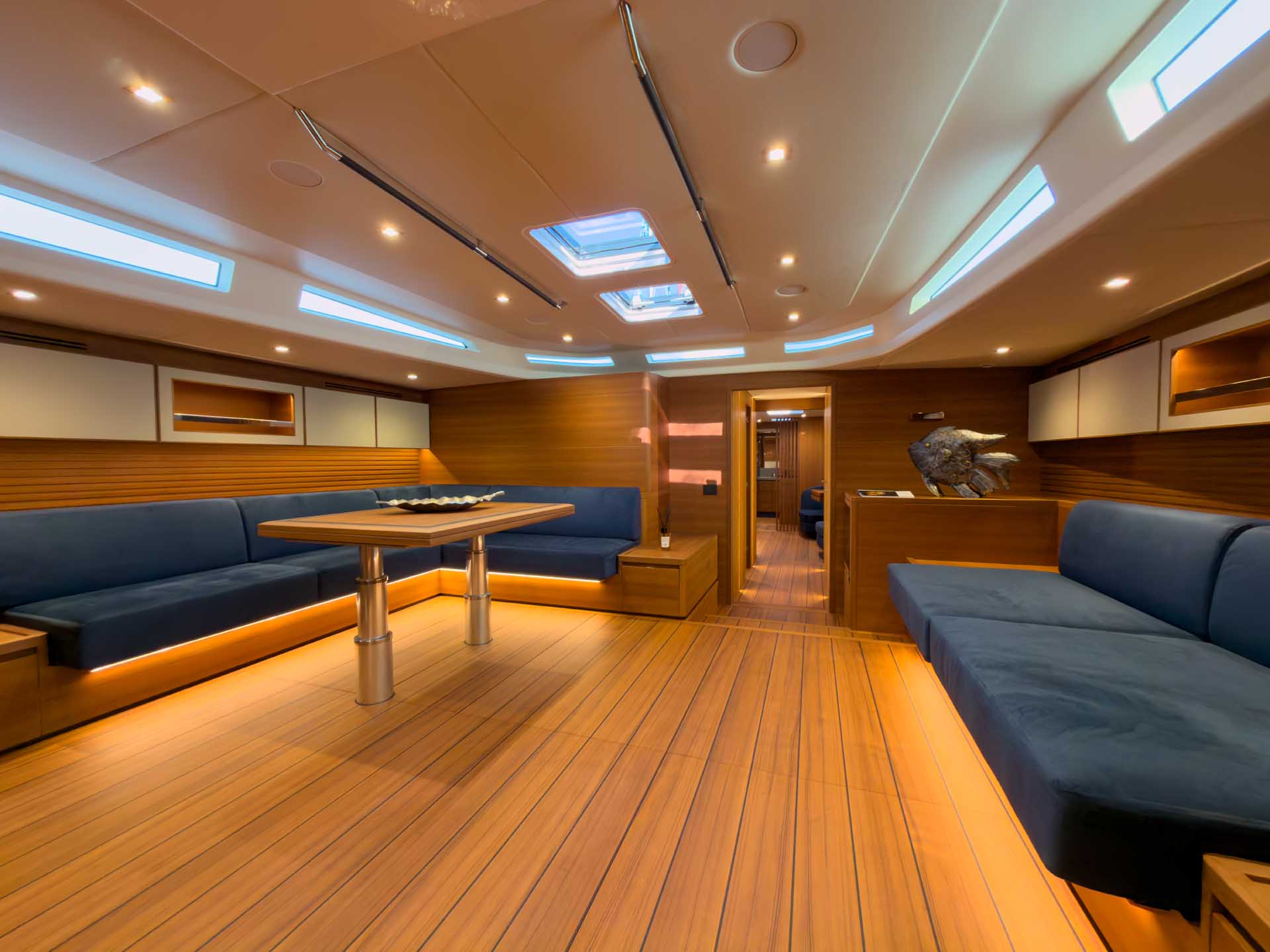 The saloon, with a teak sole, blue settees along both sides, a table and deck hatches overhead