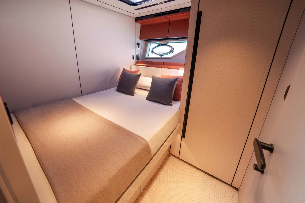 A guest cabin with a double berth against the hull side and an opening port in the window