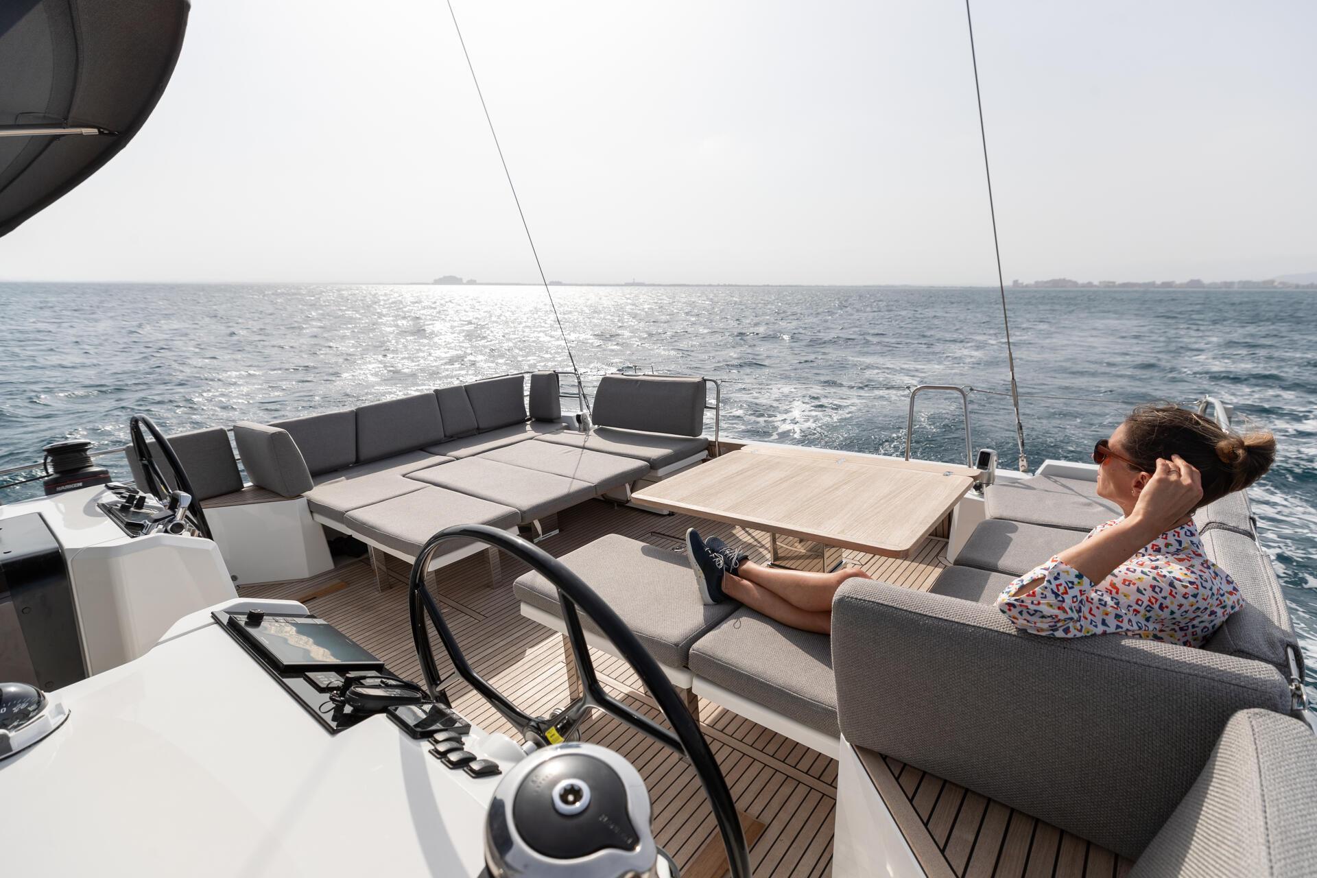 The aft cockpit table with someone seated at it, sails up beyond