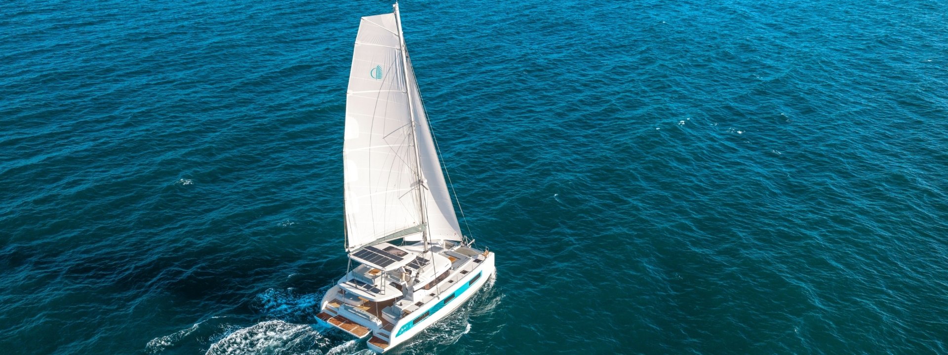 The Lagoon 47 sailing away across deep blue water, seen from above and astern