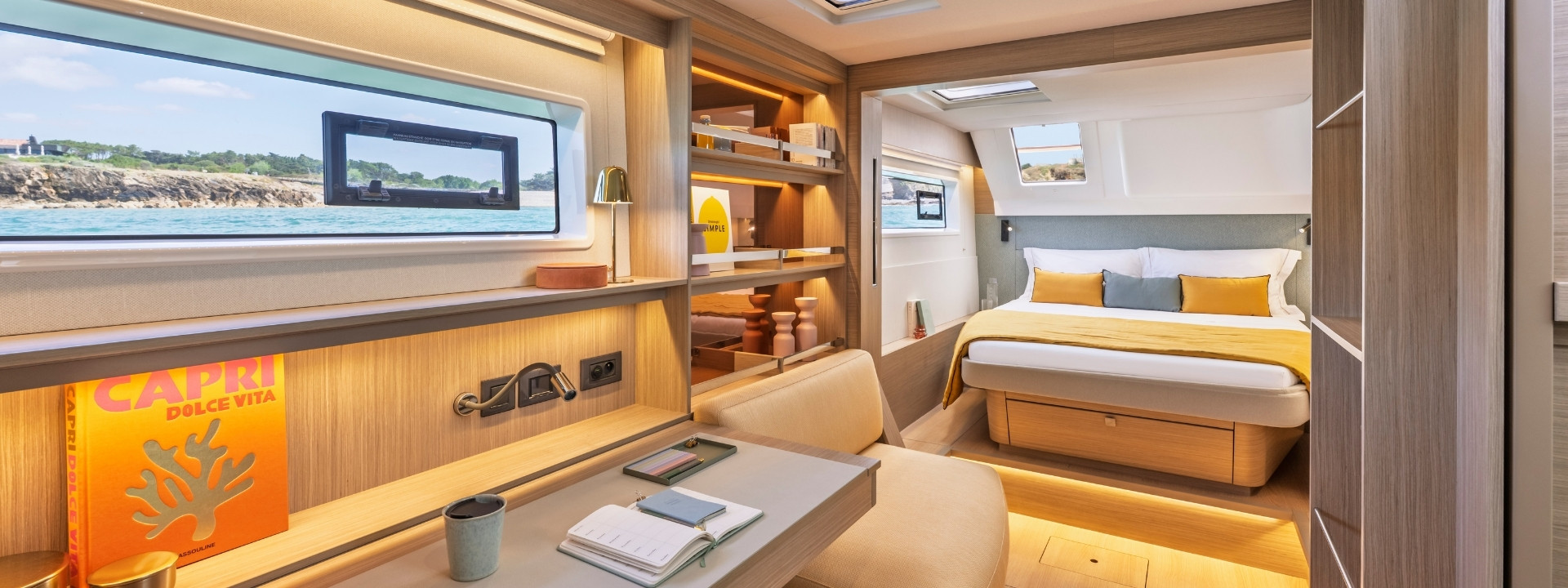 A desk with shelving under a long hull window, leading to a double cabin