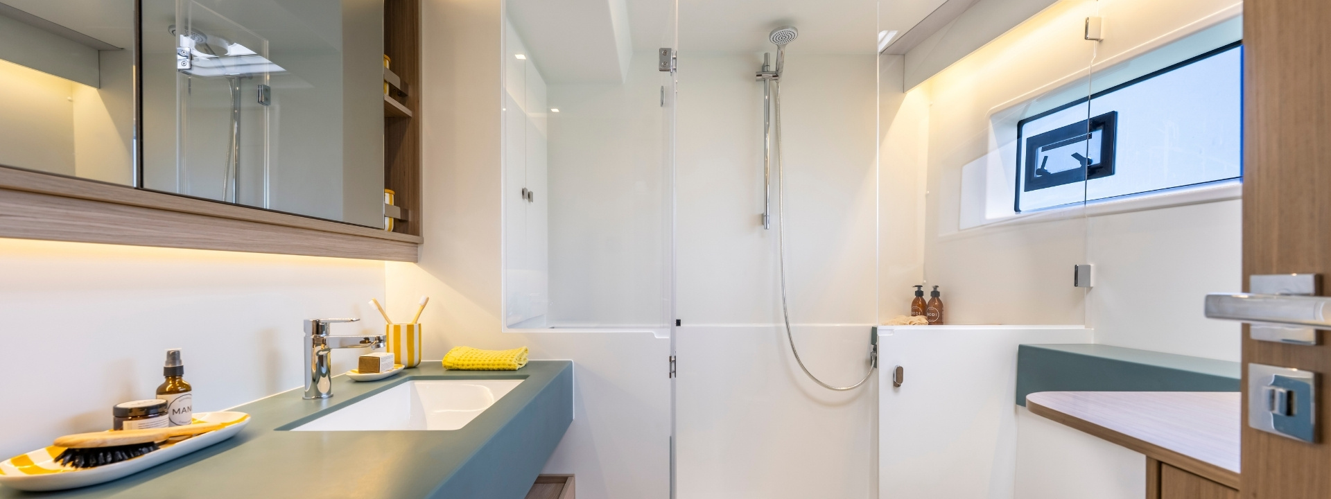 A bathroom with a glass-screened shower, a basin on a grey counter and a hull port