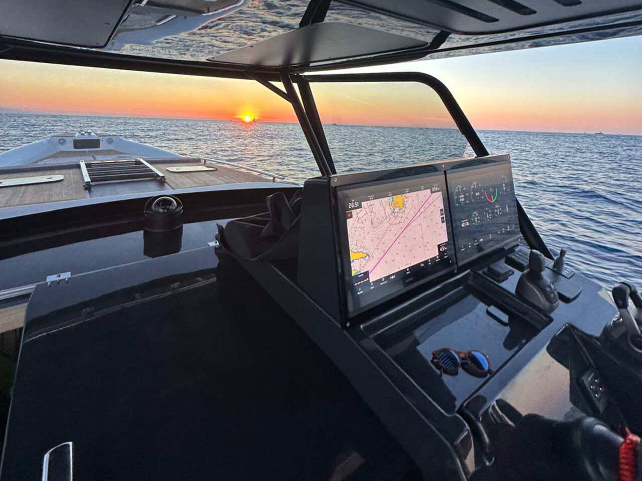 The helm at sunset, with two chartplotter screens and the wheel