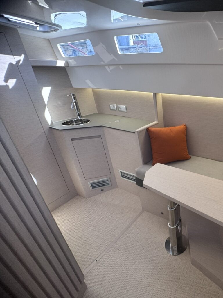 A galley counter below deck with a sink and a seat beside it