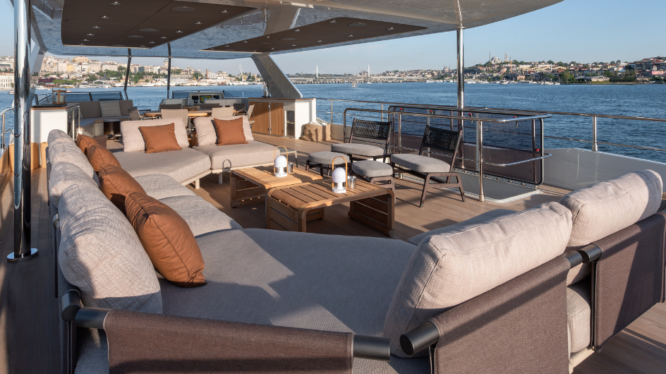 The flybridge, with a long sofa, a coffee table and the coast beyond