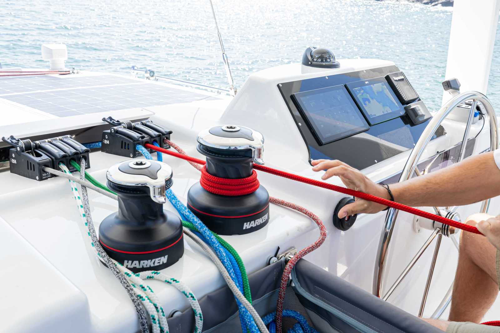 The helm station, with two Harken winches, coloured control lines led into a bank of rope clutches, a chartplotter screen and a hand on the wheel