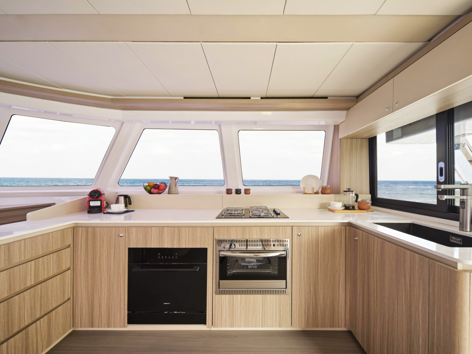 The galley, in pale wood with white worktops, a gas hob, an oven and a sink under a side window, with forward windows looking out to sea