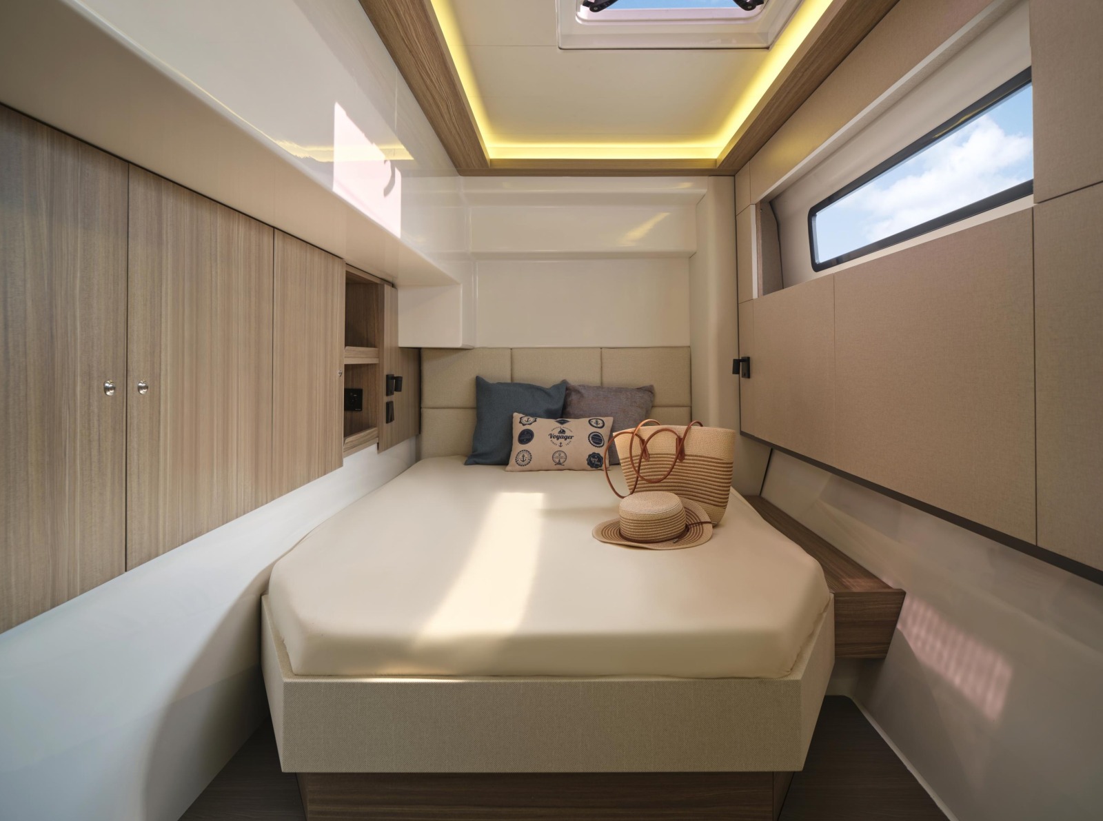 A double cabin in one hull, with a berth against a padded headboard, a wardrobe alongside, a hull window and a lit deck hatch overhead
