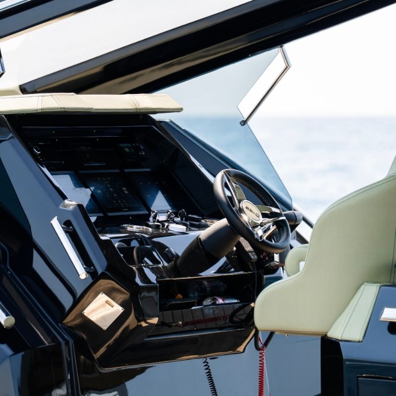 The helm station under the T-top, with a steering wheel and screens in a black console