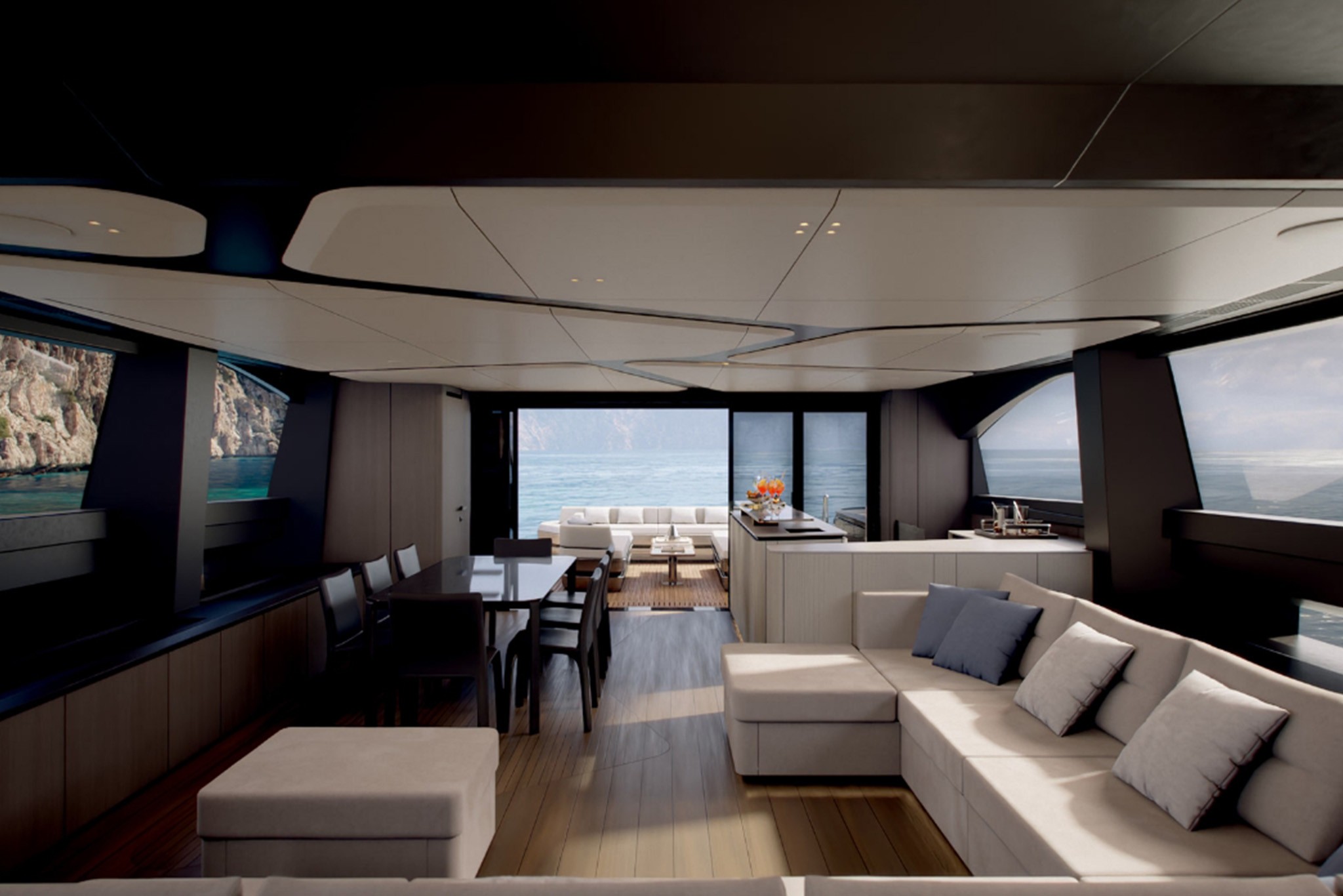 The saloon looking aft, a long pale sofa to the right and a dark dining table with eight chairs to the left, the glazed aft doors open onto the cockpit and a rocky coast beyond