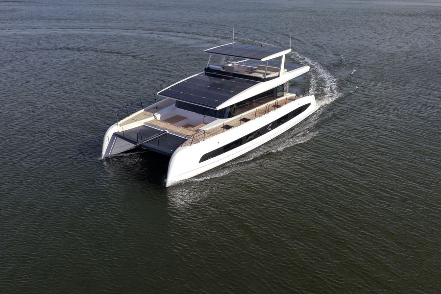 The Pioneer PY60 under way on flat grey water seen from above and astern, a white power catamaran with solar panels covering the roof and the upper deck, her two hulls leaving a light wake