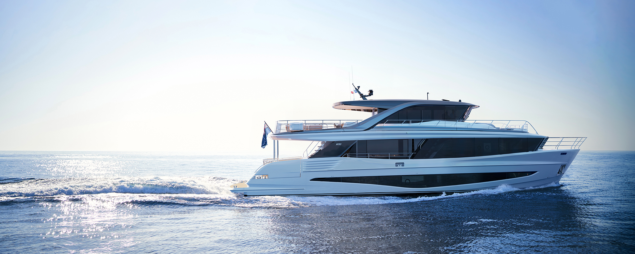 The Princess X90 under way from left to right on calm sea in hazy light, seen exactly side on, her long glazed superstructure and flybridge overhang running most of her length