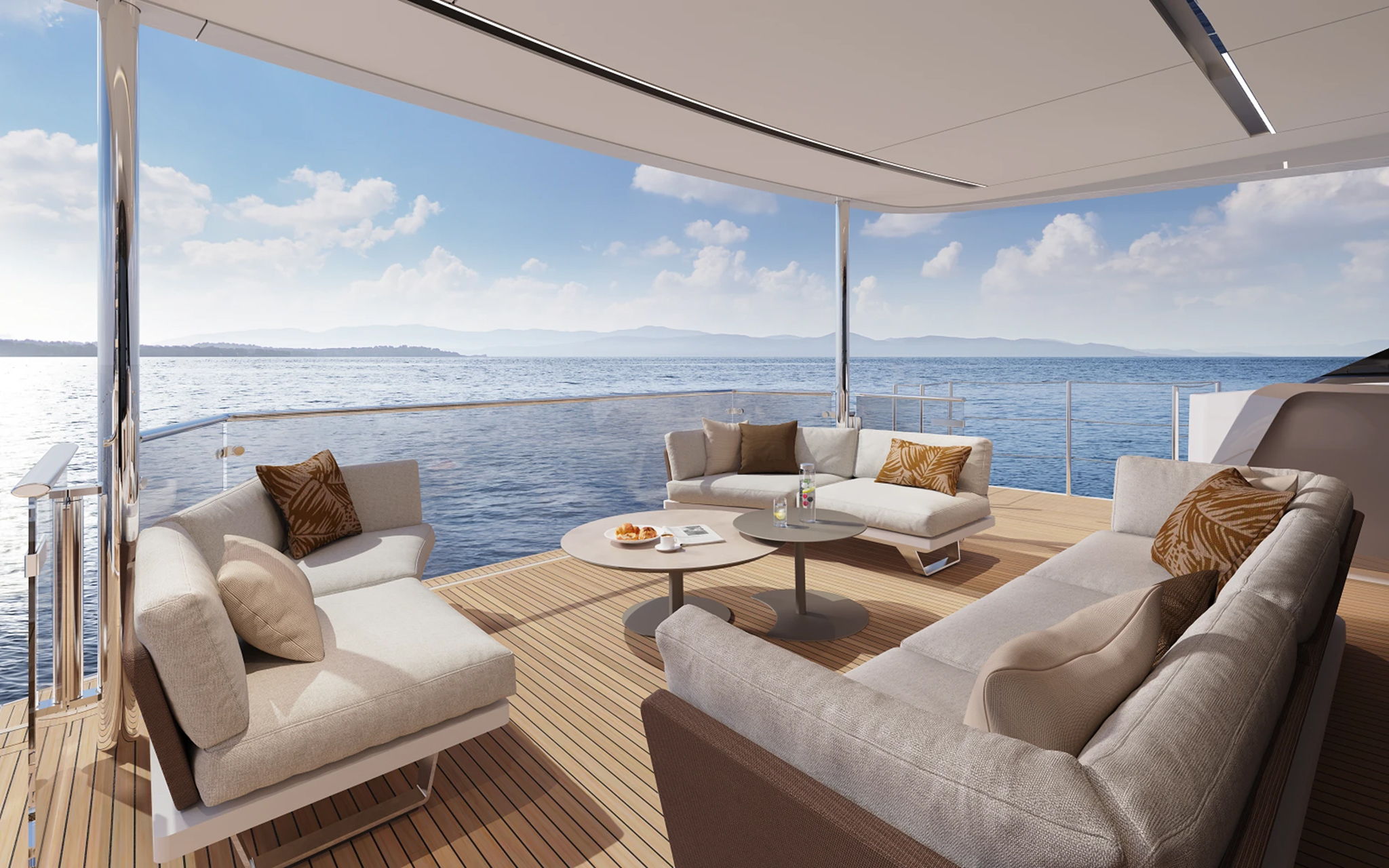 The shaded aft cockpit with an armchair and two sofas in pale fabric around low round tables on a teak deck, open to the sea on three sides