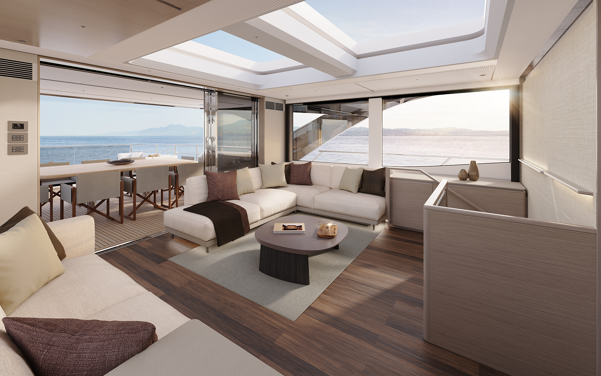 An upper lounge looking aft, an L-shaped sofa and oval table on a pale rug over dark timber flooring, with a dining table beyond and glass doors folded open to the deck