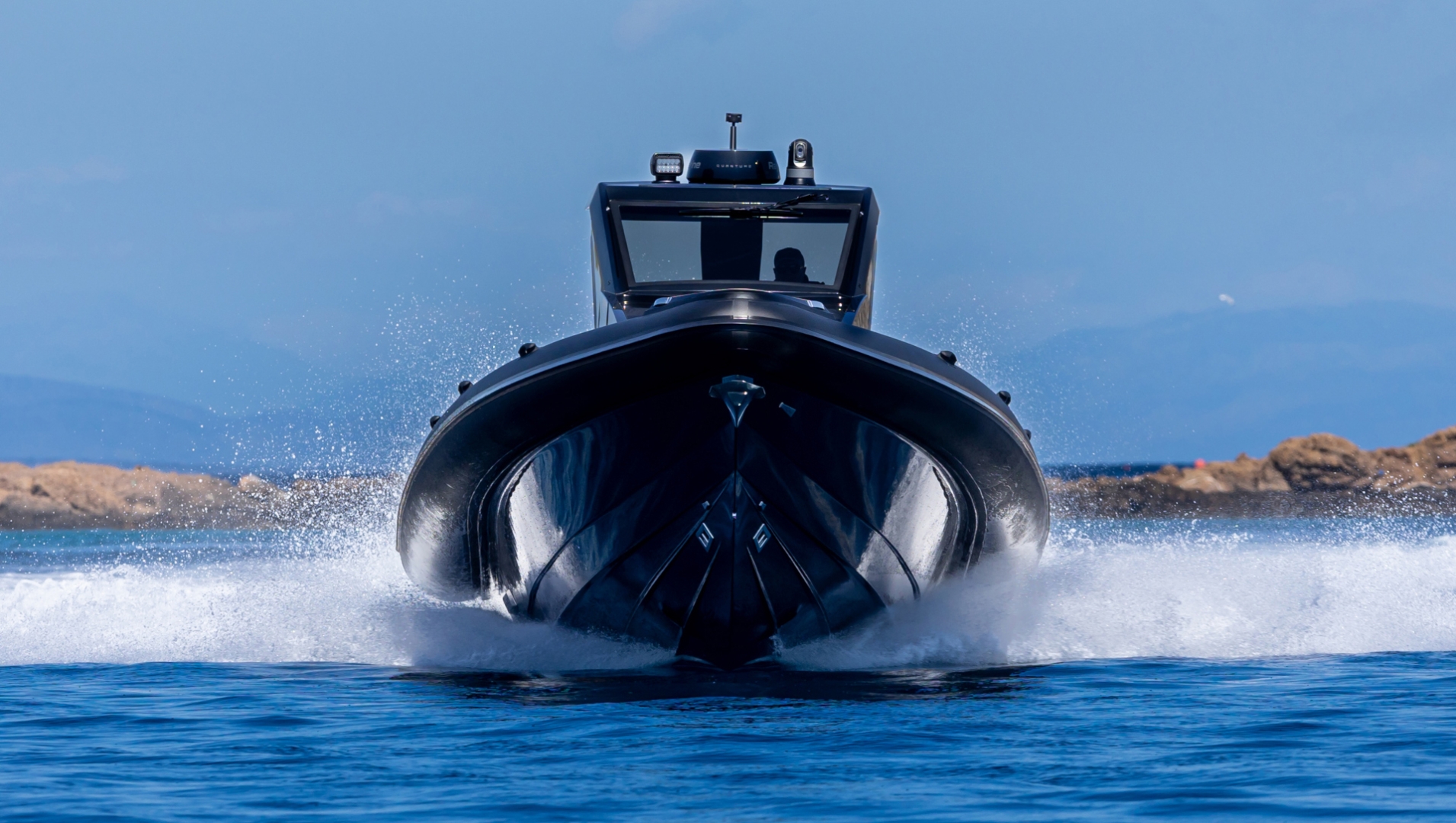 The RIBCO Venom 45 SC seen head on at speed, her black tubes and deep-V hull throwing spray either side, the helmsman just visible behind the dark windscreen under the hardtop