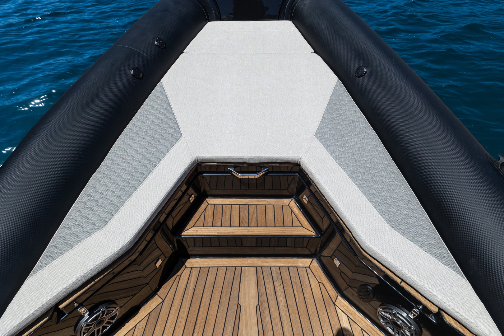 The bow seen from above, a pale sunpad across the forward tubes with teak steps down into the foredeck seating