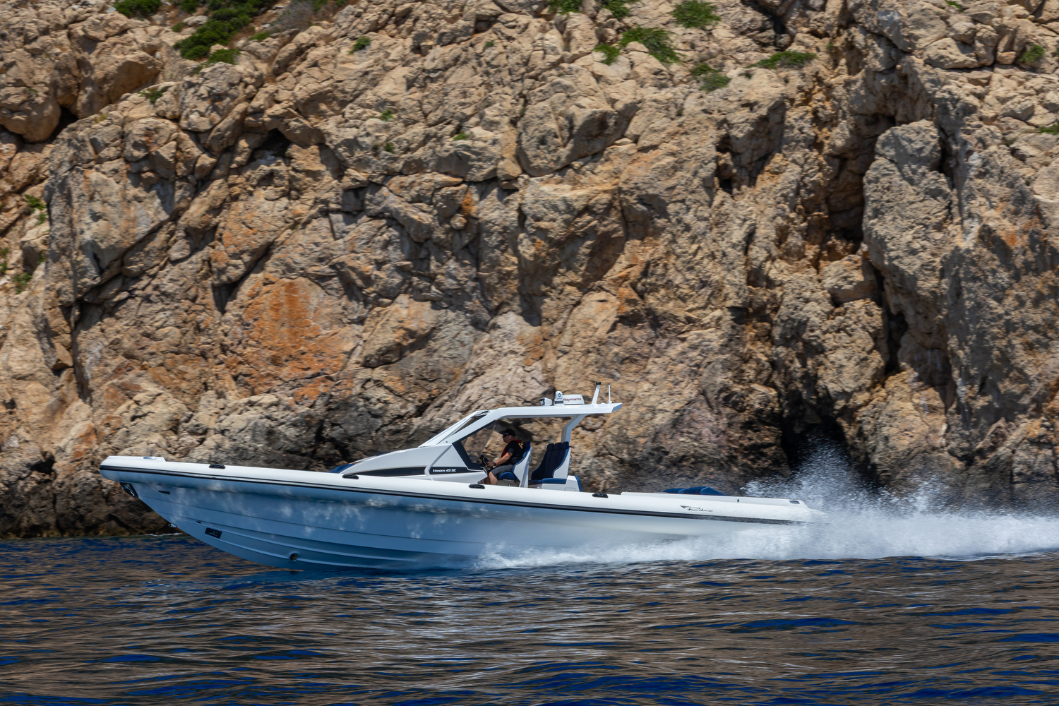 The white Venom 45 SC running in profile past a rock face, her transom clear of outboards