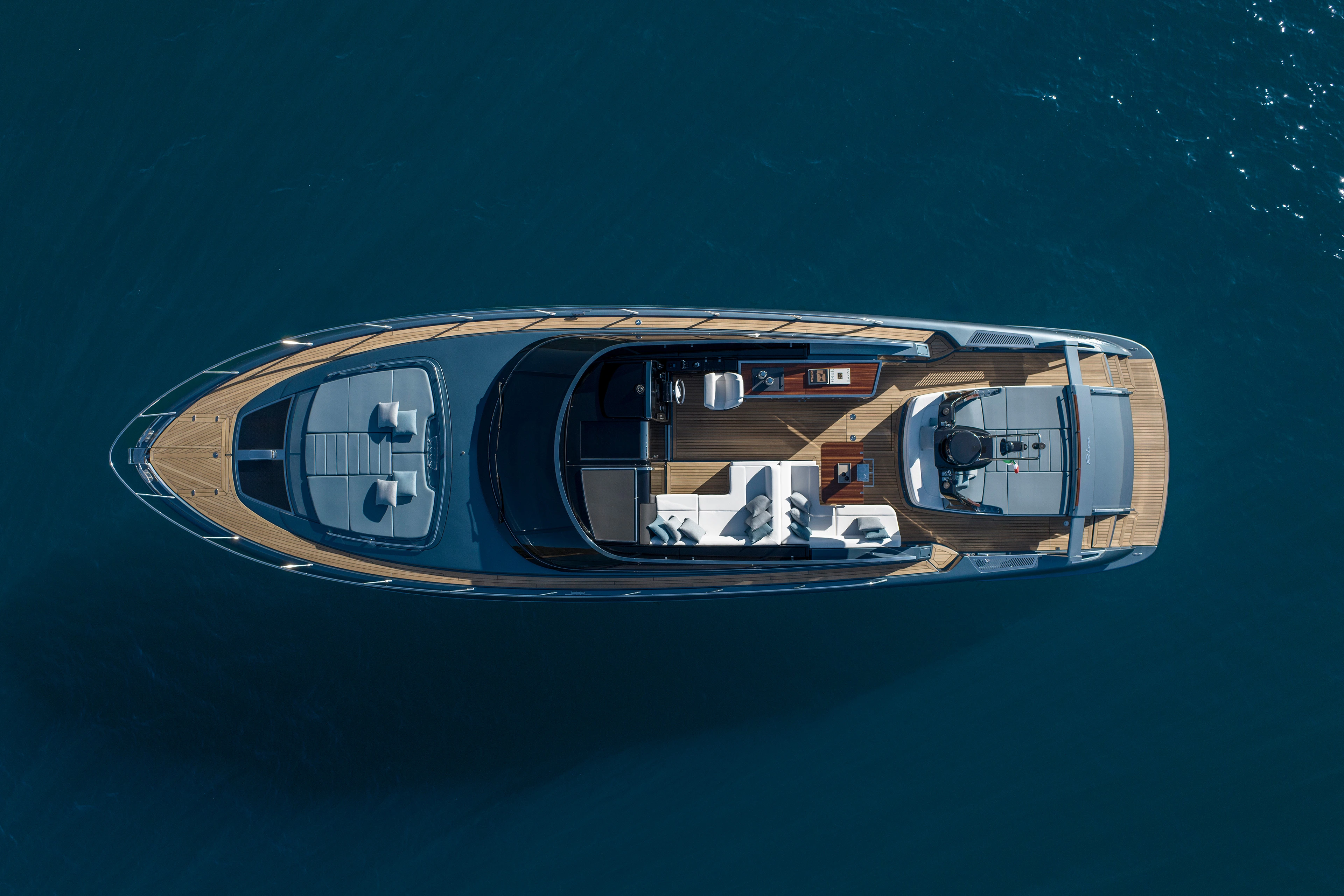 The yacht photographed from directly overhead on dark water, showing the foredeck sunpad, the teak cockpit with its seating and helm, and the aft sunbed