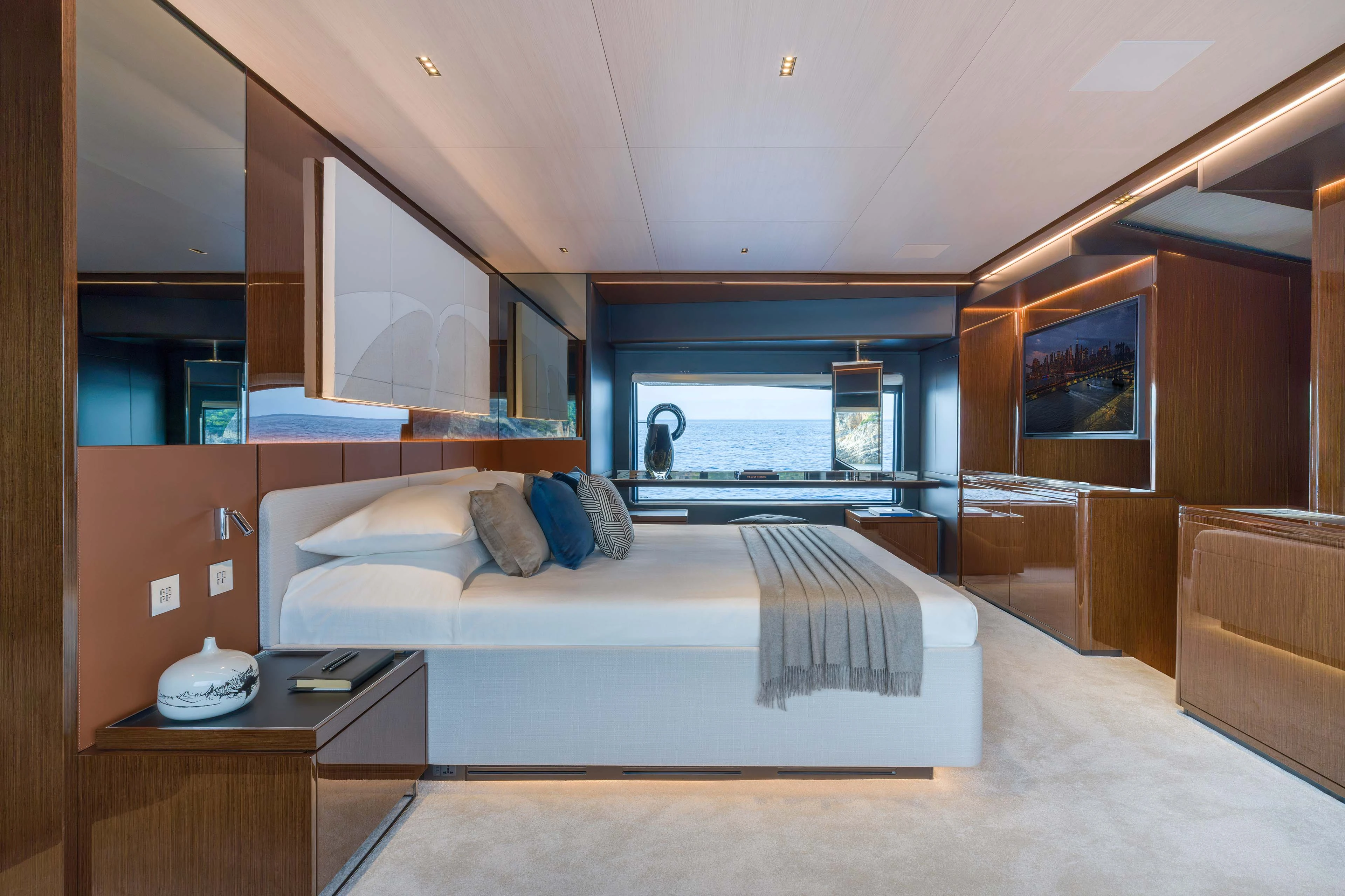 A double cabin running the width of the hull, the bed against a padded headboard with polished timber joinery either side, a long hull window at eye level and a television on the opposite wall