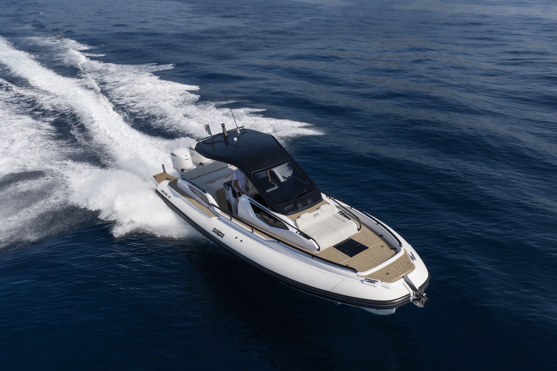 The Soleil 37 from above and ahead, turning at speed, showing the foredeck sunpad, the helm under the T-top and teak-effect decks