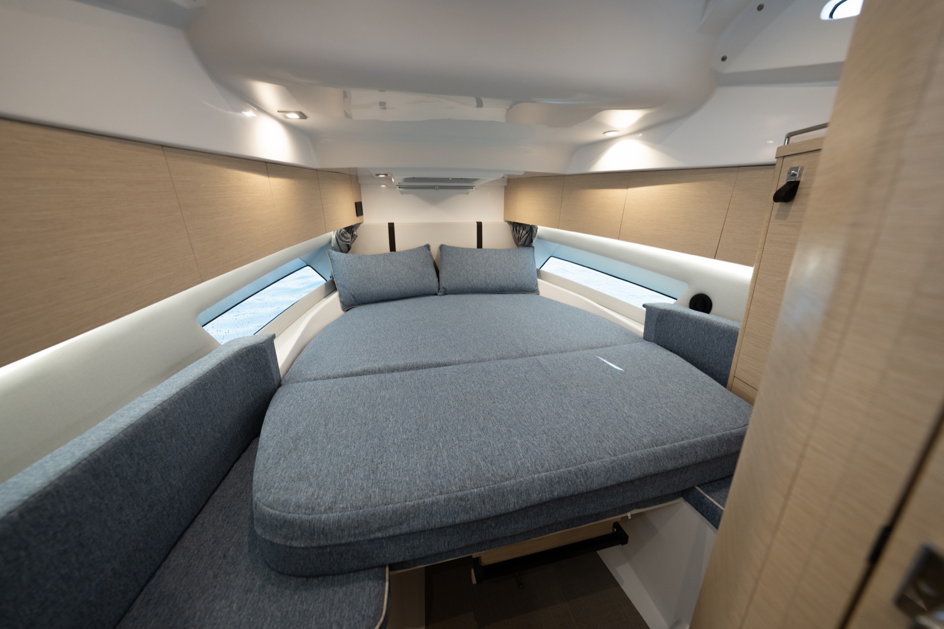 The cabin of the Soleil 37, a double berth in grey upholstery filling the bow, with hull windows either side