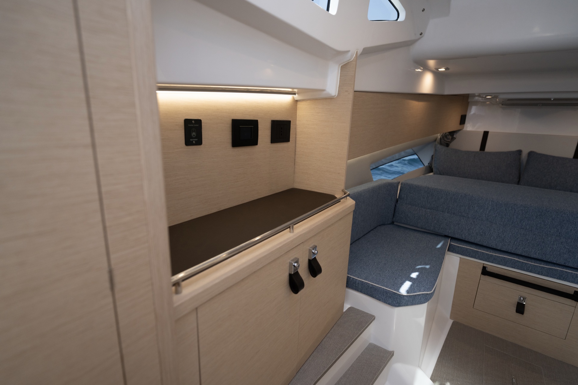 Inside the Soleil 37 cabin, a light-oak cabinet and counter to the left and the grey bow berth beyond