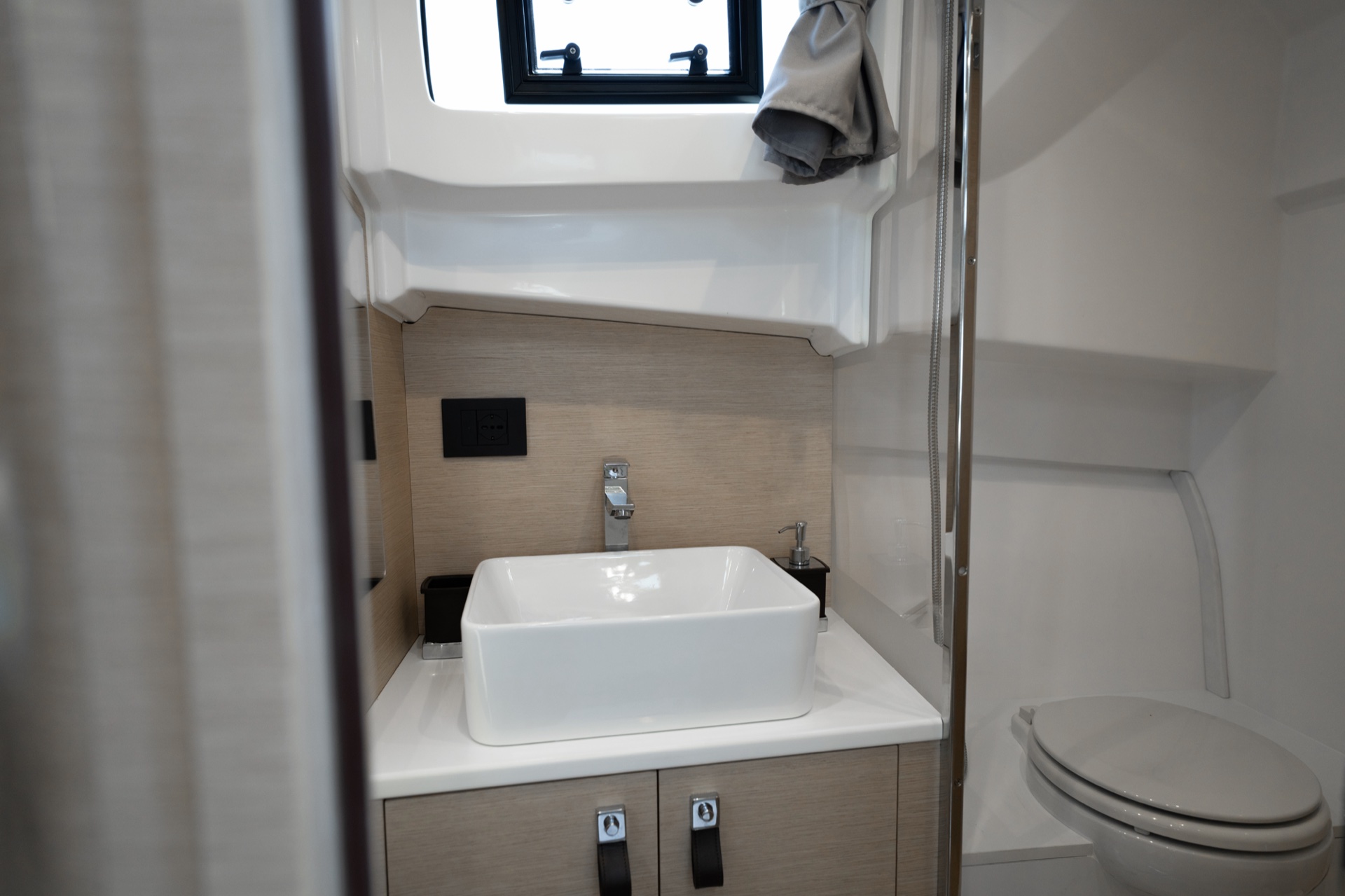 The washroom of the Soleil 37, a square basin on a light-oak vanity, a toilet and a porthole above