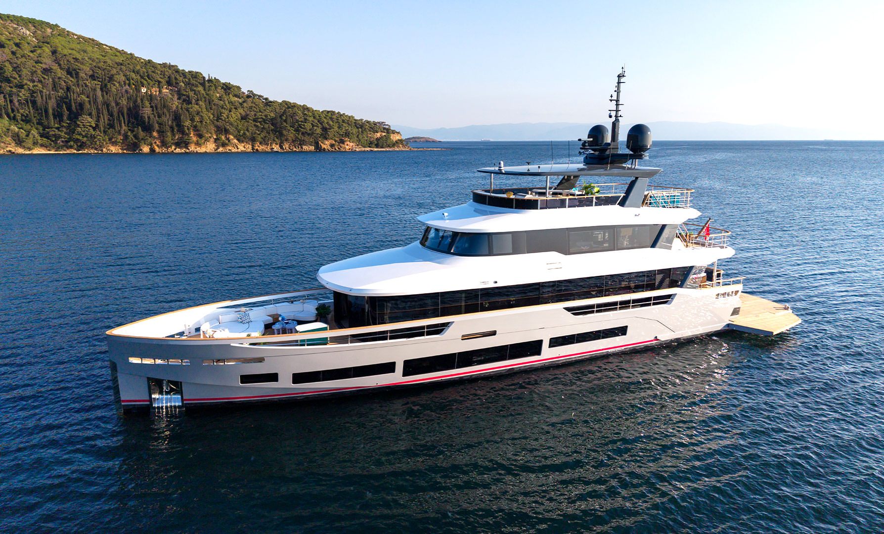 The Sirena 118 lying off a wooded headland, her aft balcony folded out