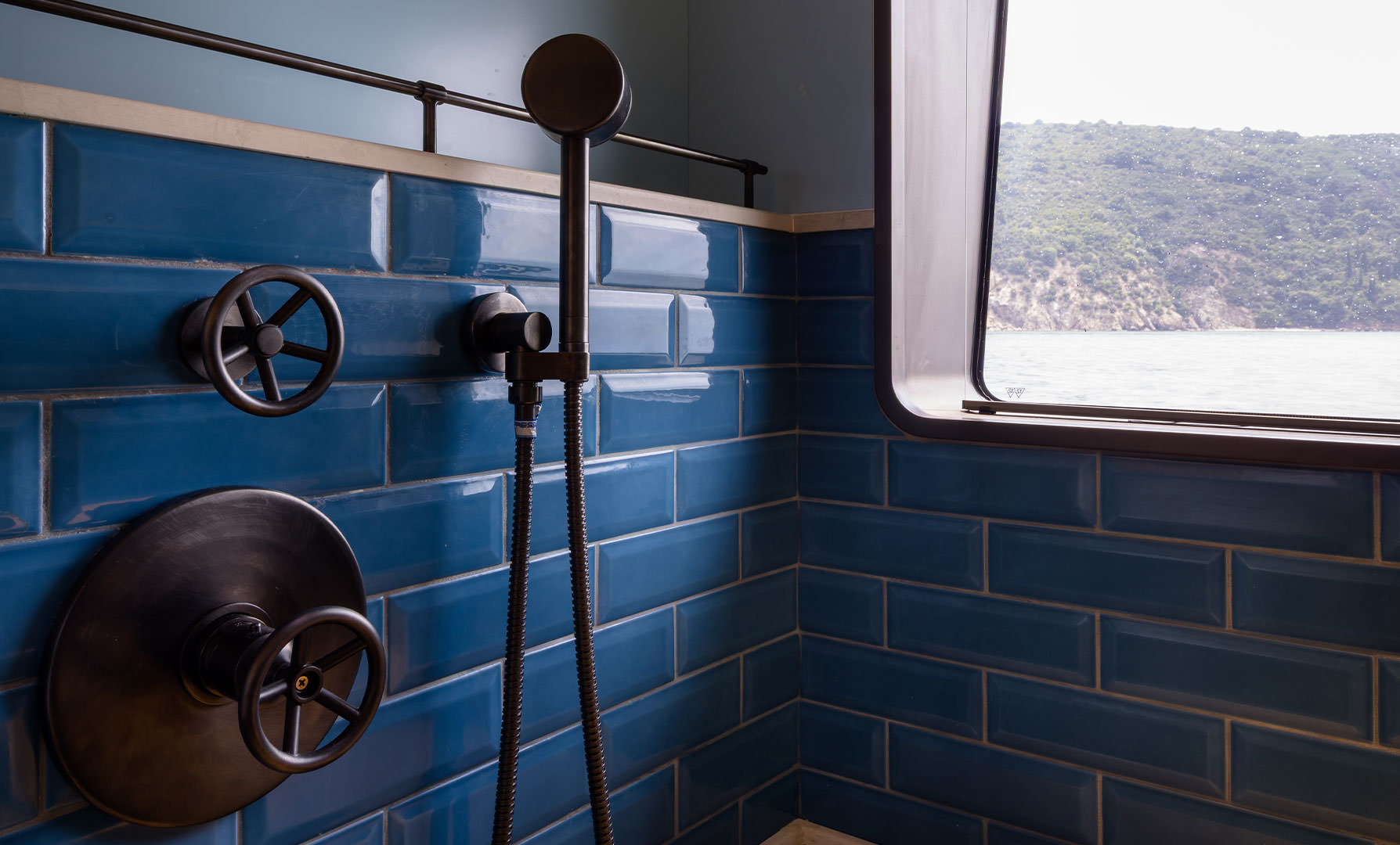 A shower compartment lined in dark blue tile with bronze fittings
