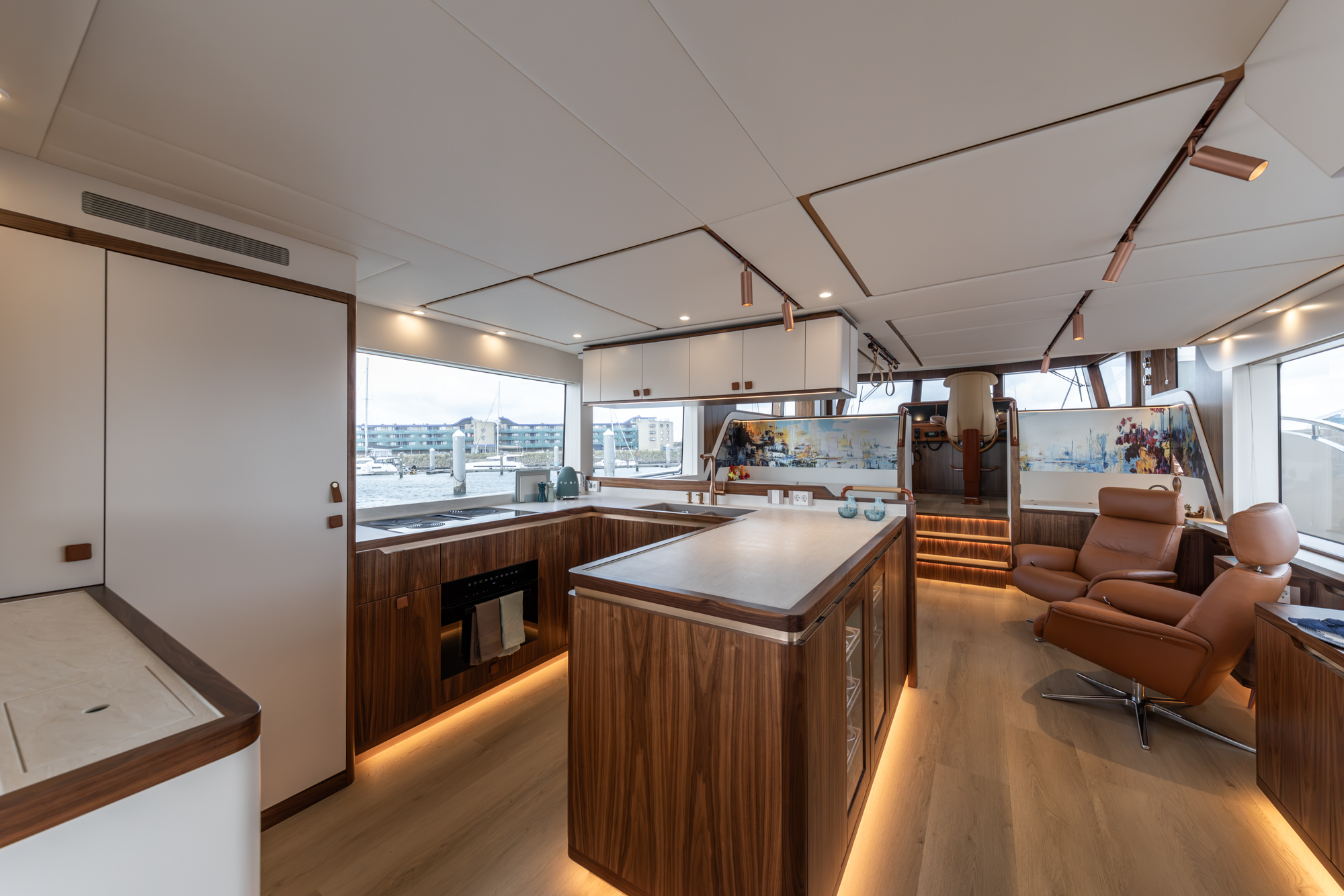 A saloon looking forward, with a galley island and leather armchairs