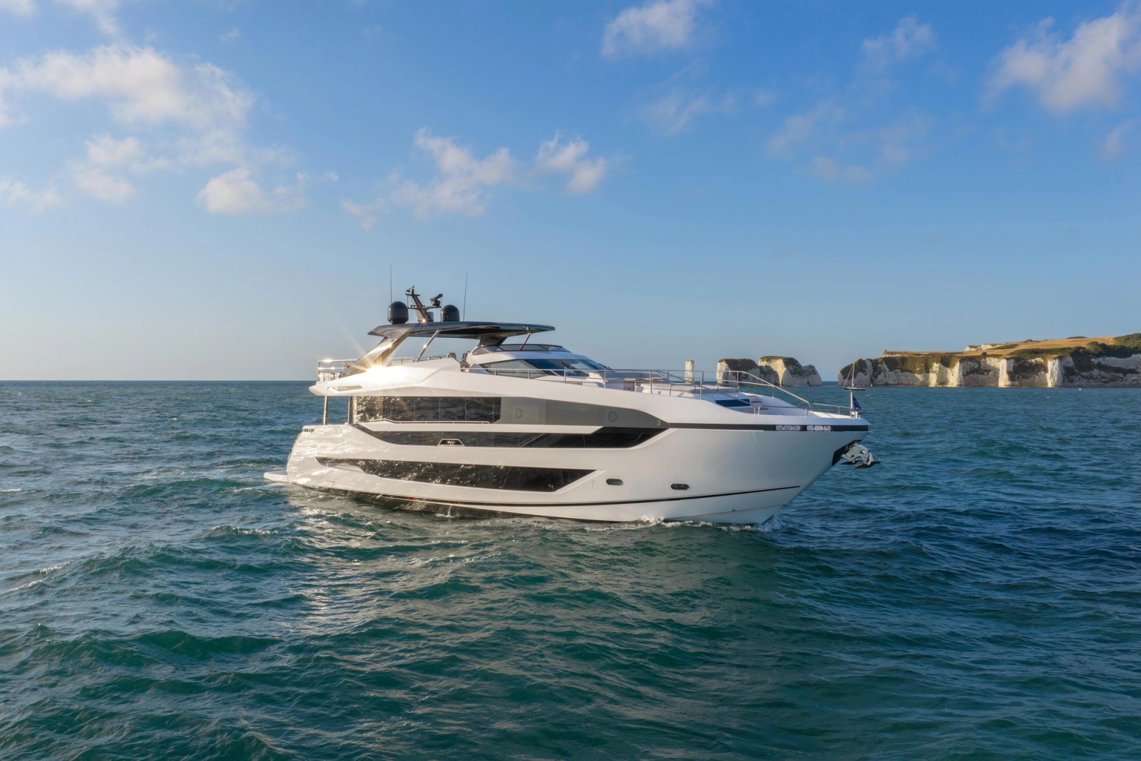 The Manhattan 94 seen from ahead and off to one side, her raised pilot house and dark hardtop standing above a white hull, chalk cliffs in the distance