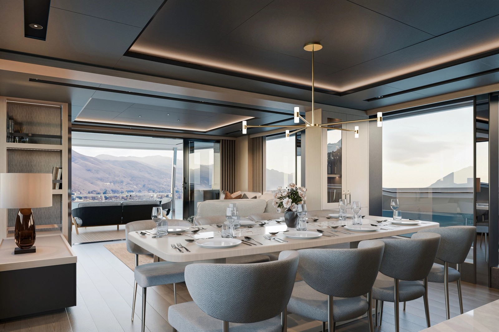 The dining table laid for a meal with upholstered chairs around it under a slim pendant light, the saloon seating and open glass doors to the side deck beyond