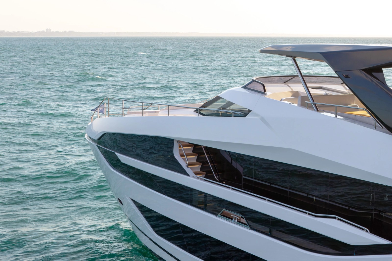 A close view of the bow and superstructure from abeam, showing the stepped side decks, the dark glazing and the staircase up to the flybridge under its hardtop