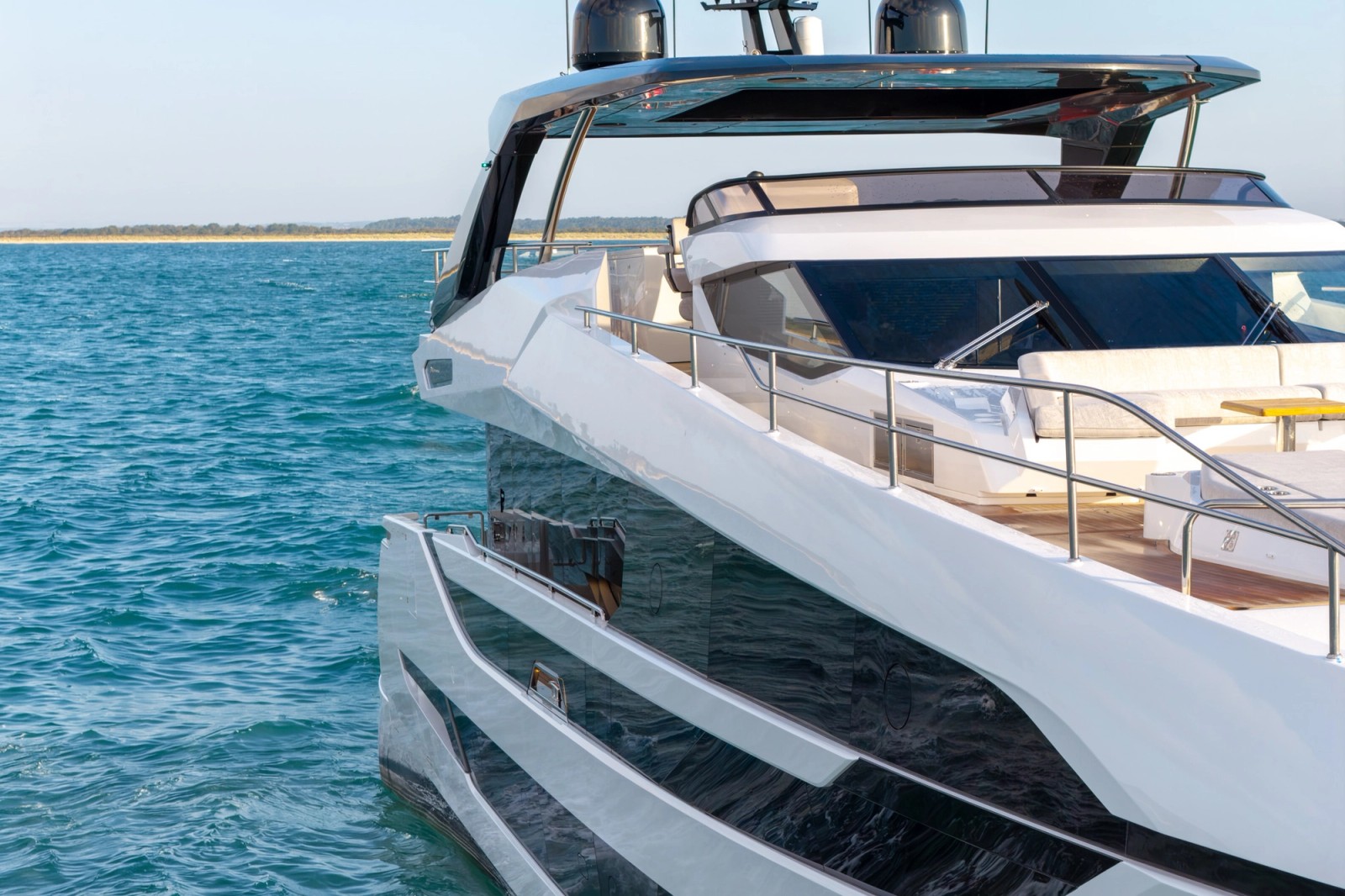 The flybridge overhang and hardtop seen from close astern and below, satellite domes above and the aft deck seating and teak visible beneath
