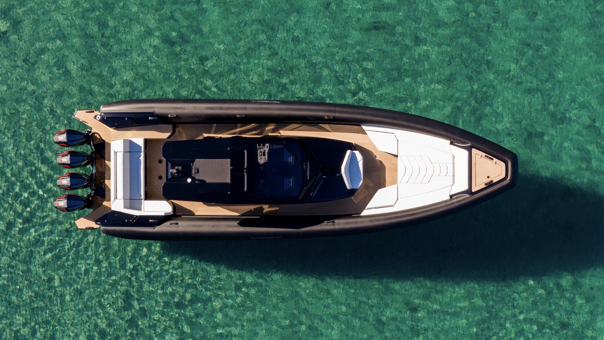 Straight down from above at rest in clear green water, showing the walk-around deck and the quad outboards