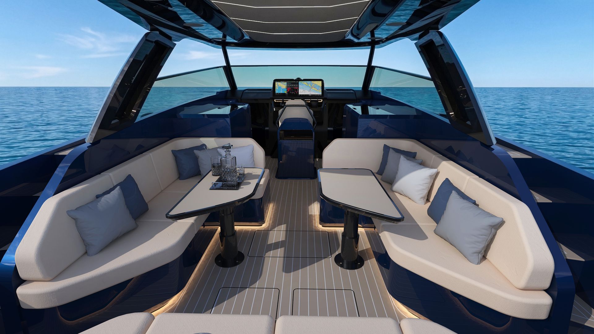 The cockpit looking forward under the open hardtop, two facing sofas with folding tables on a teak deck, the helm console and its wide screen beyond, open sea on both sides