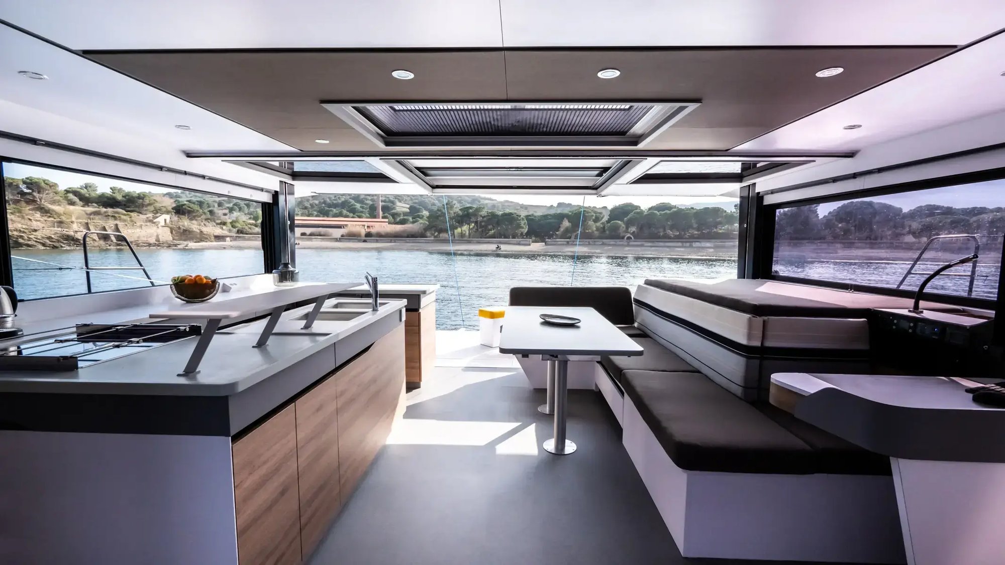 The saloon looking forward, with a galley island and a dining table under wide windows